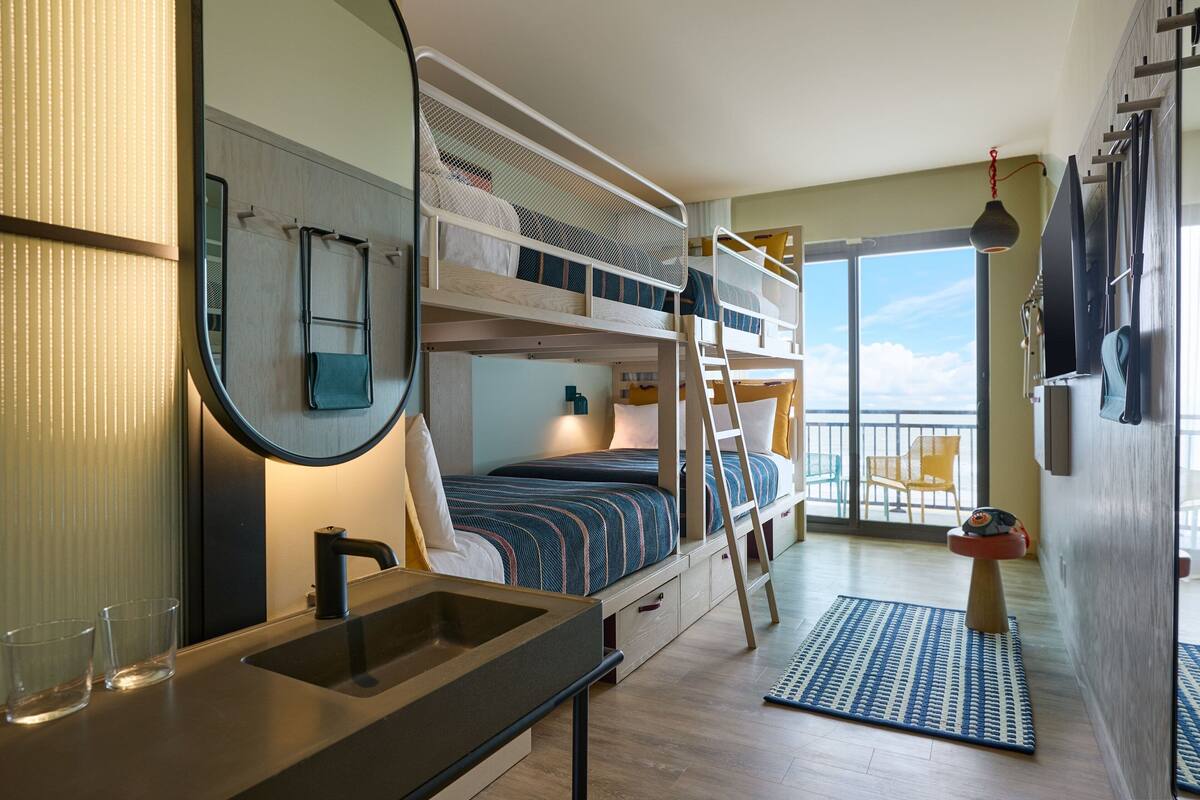 A bunk bed room with a sink, mirror, and a view of the balcony.