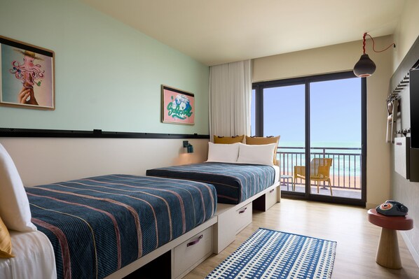 Habitación de hotel con dos camas, un balcón con una silla y vista al mar.