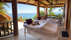 A balcony with two beds, a ceiling fan, and a view of the ocean.