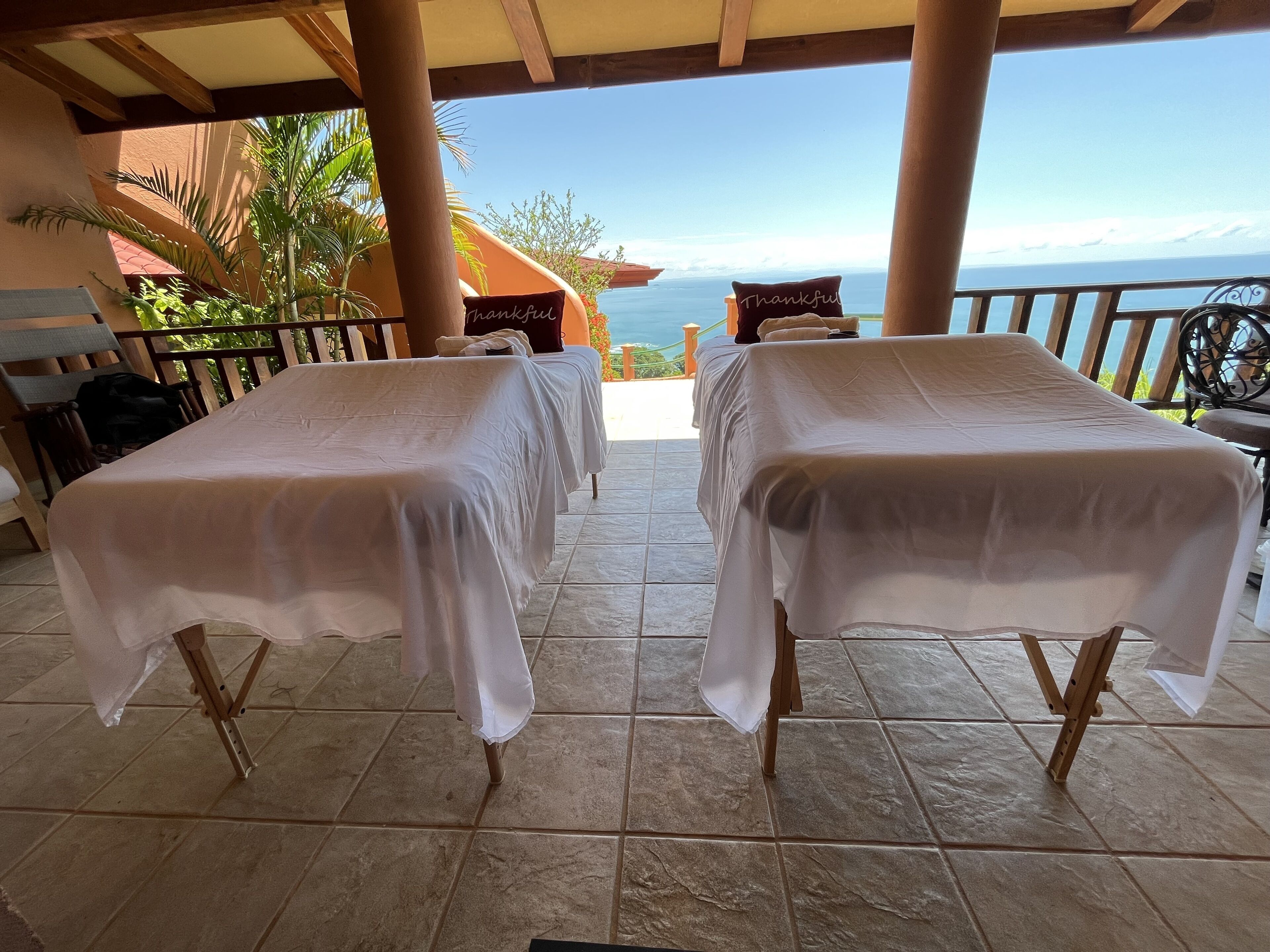 Twee massagetafels met witte hoezen, een houten bankje en uitzicht op de oceaan.