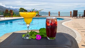 A table with a drink and a flower by a poolside with a view of the mountains.