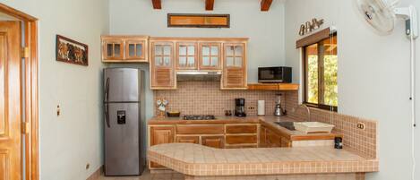 Una cocina con armarios de madera, un refrigerador de acero inoxidable, una isla grande con taburetes, un microondas y un ventilador.
