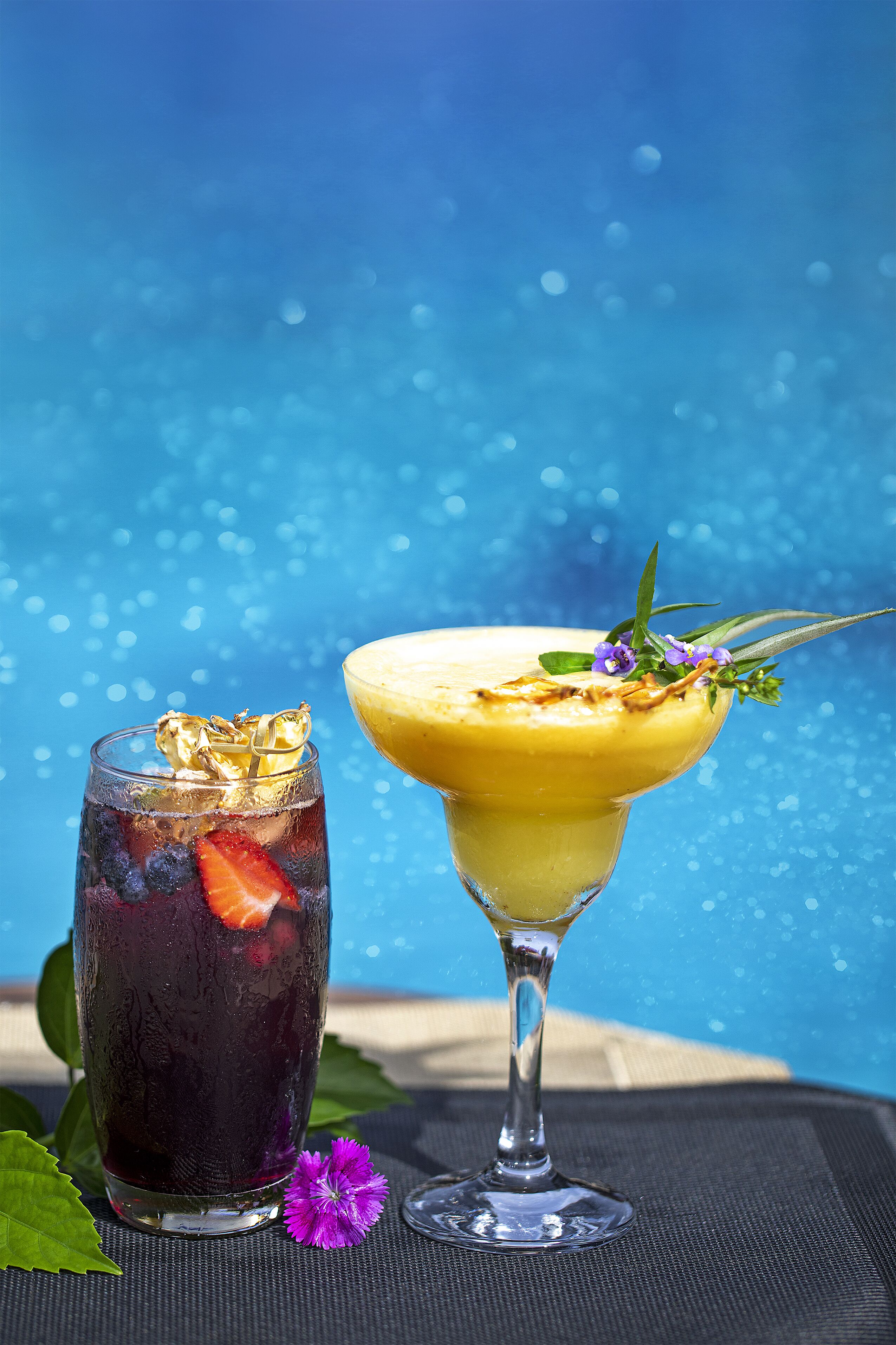 Two drinks, one in a tall glass and one in a martini glass, with a blue background.
