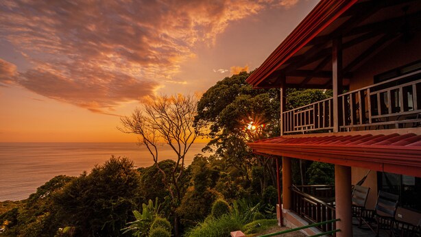 A coastal property with a balcony overlooking the sea, surrounded by lush greenery.