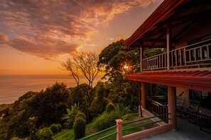Ein Küsteneigentum mit einem Balkon mit Blick auf das Meer, umgeben von üppiger Vegetation.