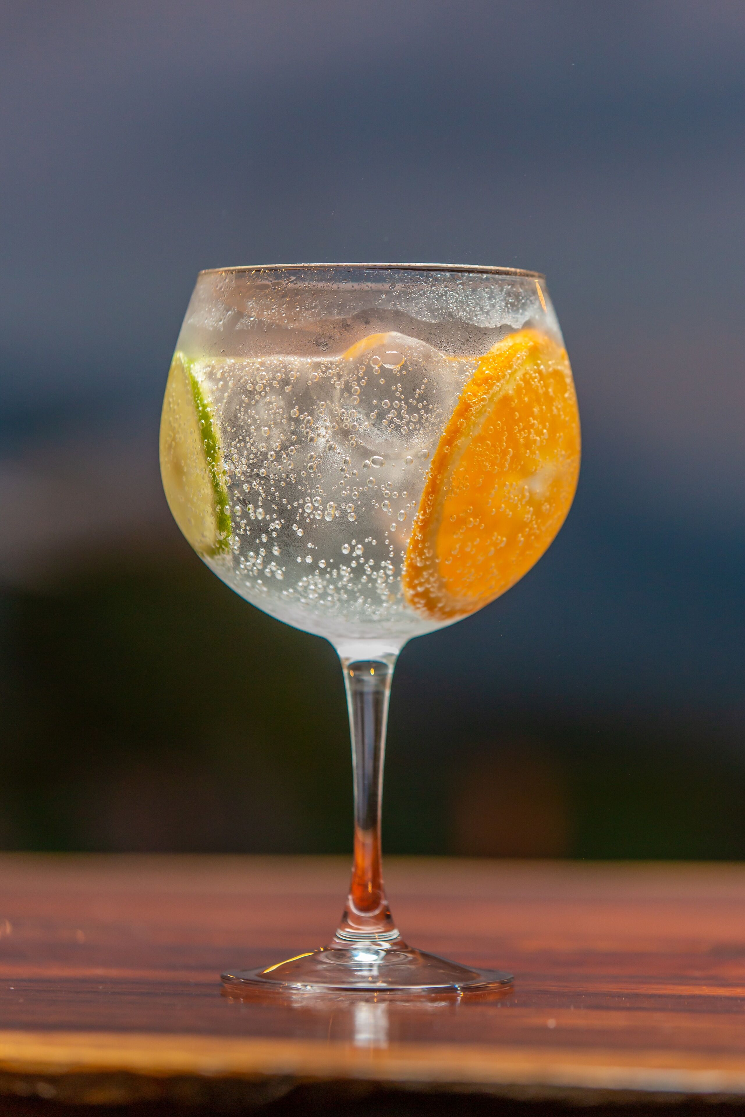 A clear glass with ice cubes, lime, and an orange slice.