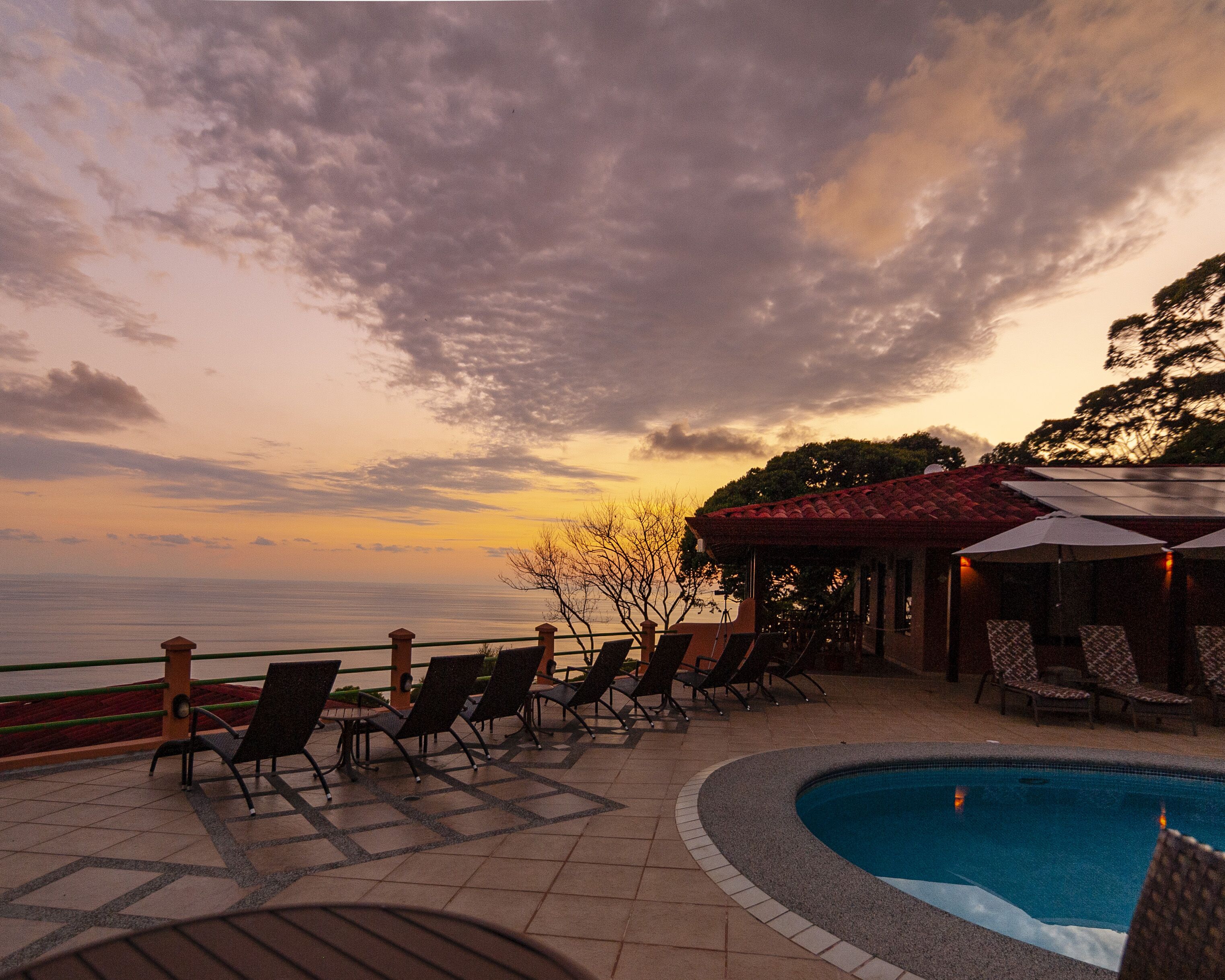 Ein Poolbereich mit Liegestühlen und einer überdachten Lounge, mit Blick auf ein Gewässer bei Sonnenuntergang.