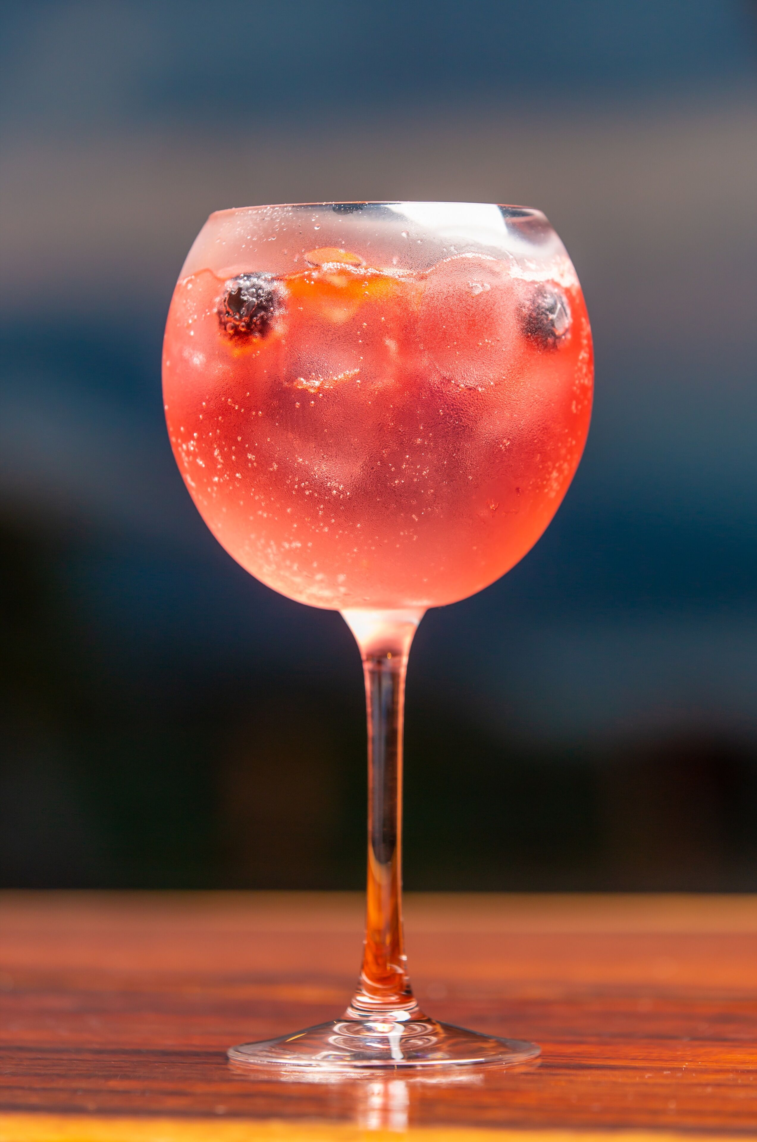 A cocktail glass with ice cubes and fruit on a wooden surface.