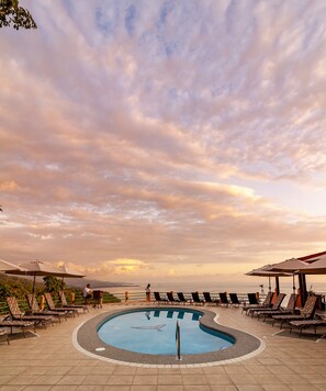 A pool area with lounge chairs and umbrellas, surrounded by a tiled deck.