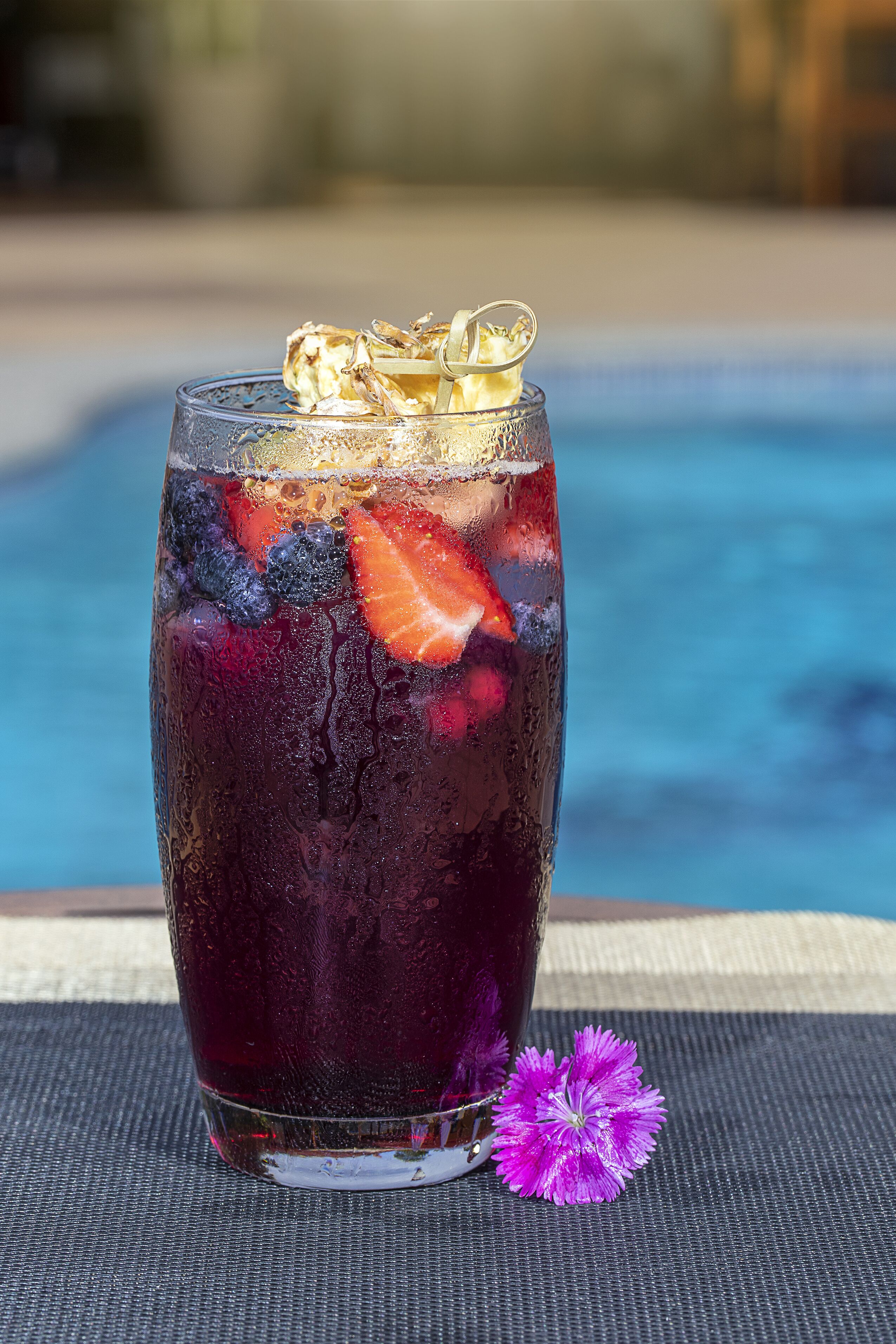 Een glas met een verkoelend drankje, fruit en een decoratief voorwerp, op een tafel in de buurt van een zwembad.
