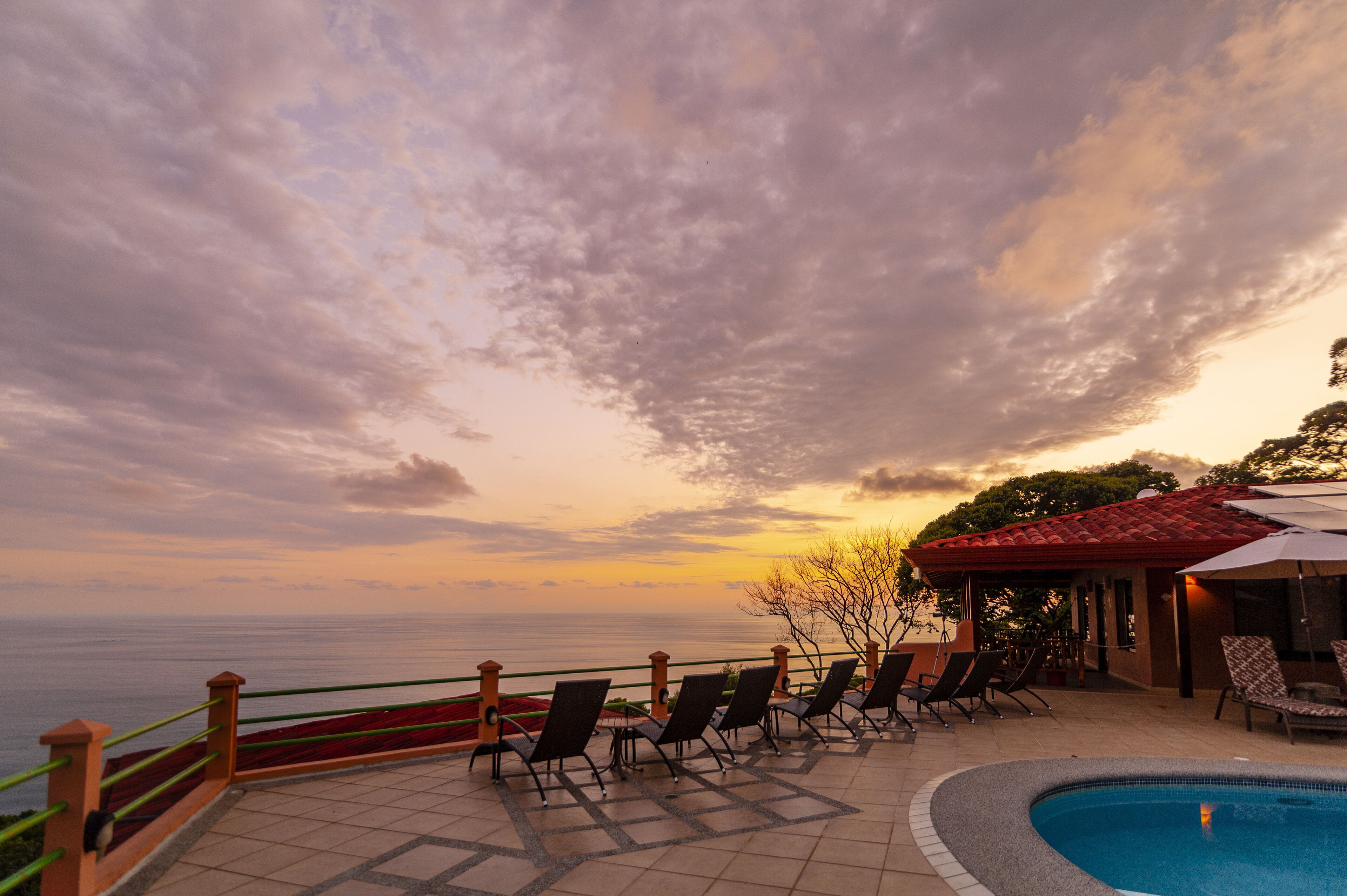 Area piscina con poltronne relax e vista sul mare al tramonto.