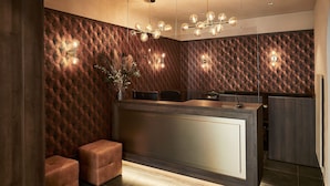 A modern reception area with a wooden textured wall, a central desk, and two cushioned seating areas. - Piazza Ascona Hotel & Restaurants (Ascona)