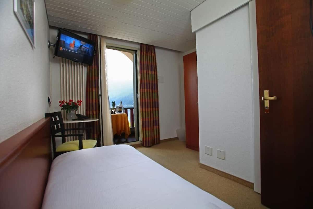 Une chambre d’hôtel comprenant un lit, un bureau avec une chaise, un téléviseur fixé au mur et une porte.