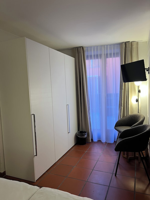 A hotel room with a bed, a wardrobe, a chair, a TV, and a window with curtains. - Piazza Ascona Hotel & Restaurants (Ascona)
