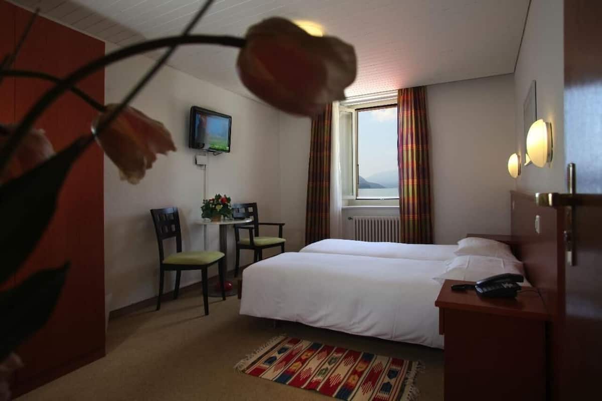 Une chambre d’hôtel avec deux lits, un bureau avec une chaise, un téléviseur fixé au mur et une fenêtre avec des rideaux.