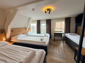 Ein Hotelzimmer mit drei Betten, einem Schreibtisch und Blick auf Gebäude.