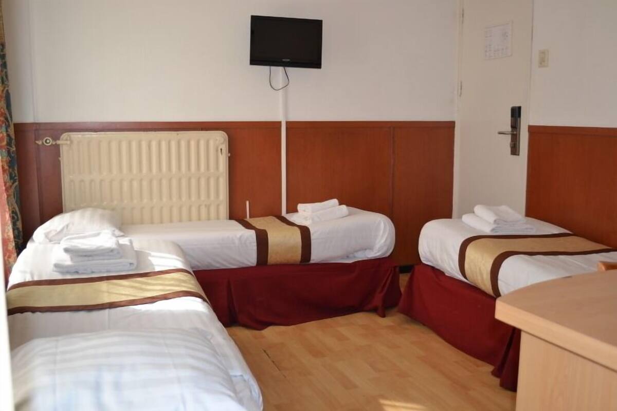 Habitación de hotel con dos camas, suelo de madera, radiador, televisión montada en la pared y una puerta con cerradura.