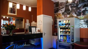Zona de recepción de un hotel con mostrador, refrigerador y máquina expendedora.