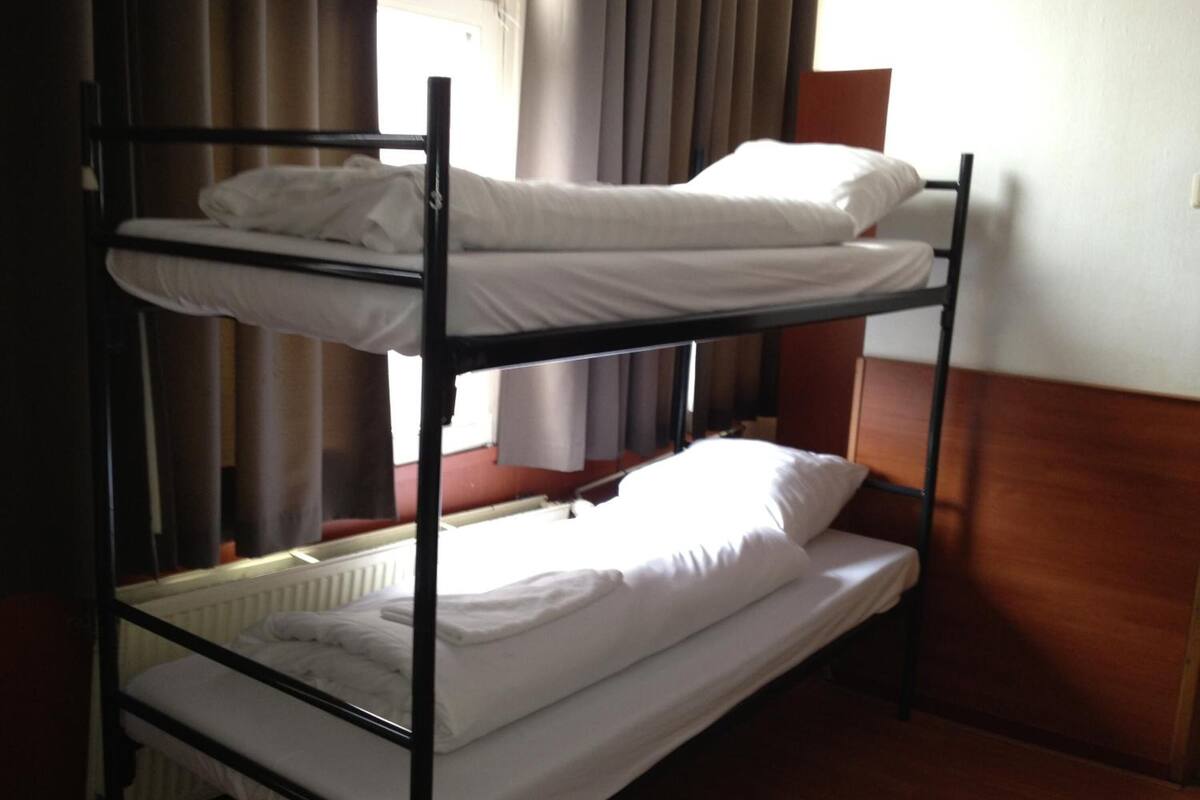 Une chambre avec un lit superposé, dotée de draps blancs et d’une tête de lit en bois.