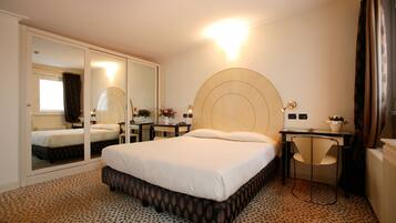A hotel room with a large bed, a desk, a chair, a mirror, and a small table with a plant.