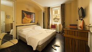Habitación de hotel con cama, escritorio, silla, televisor y ventana con cortinas.