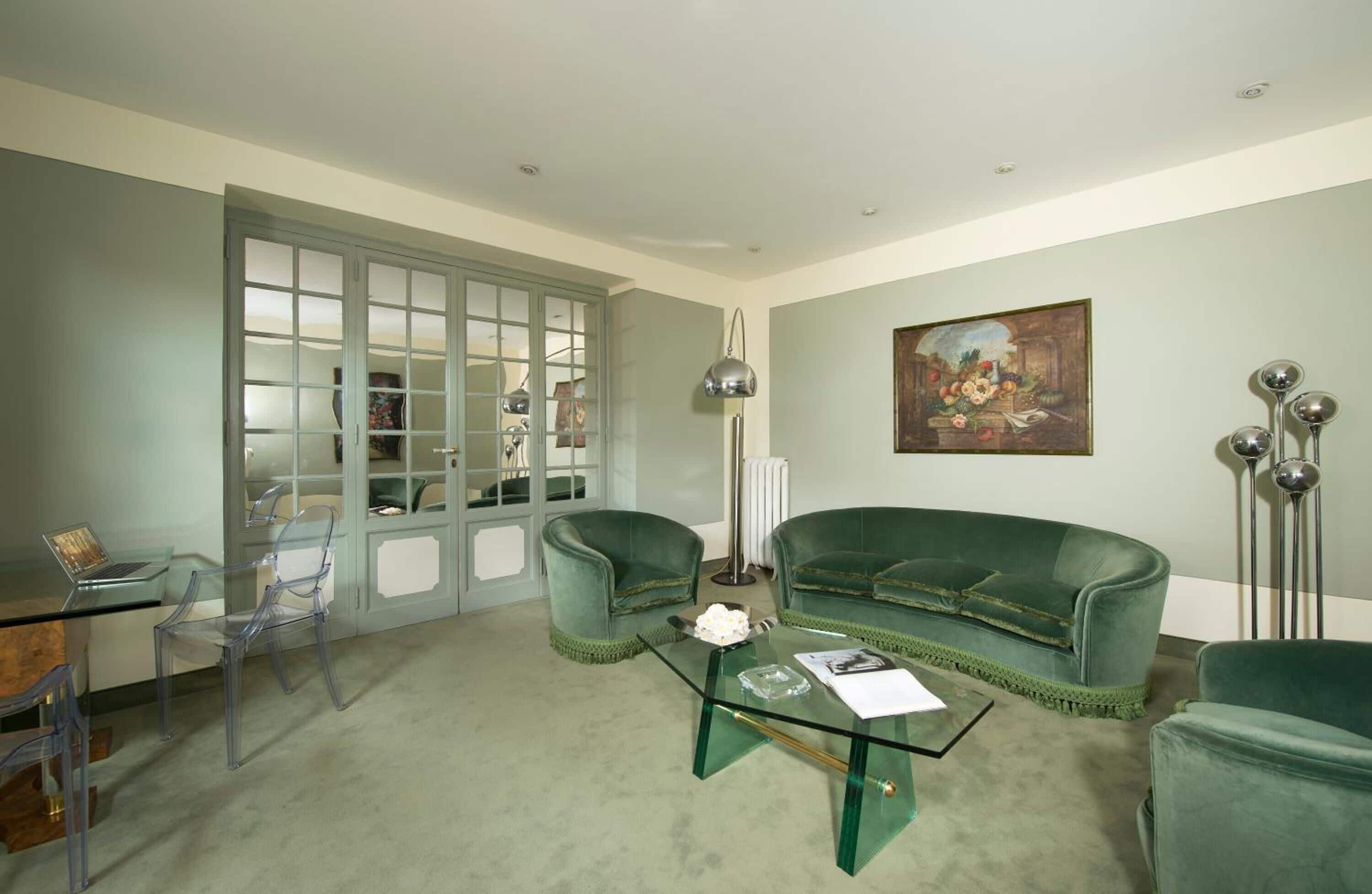 A living room with a green sofa, clear chairs, a glass coffee table, and a painting on the wall.