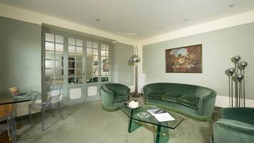 A living room with a green sofa, clear chairs, a glass coffee table, and a painting on the wall.