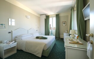 Una camera d'albergo con un letto, un comodino, una lampada e vista all'esterno da una finestra.