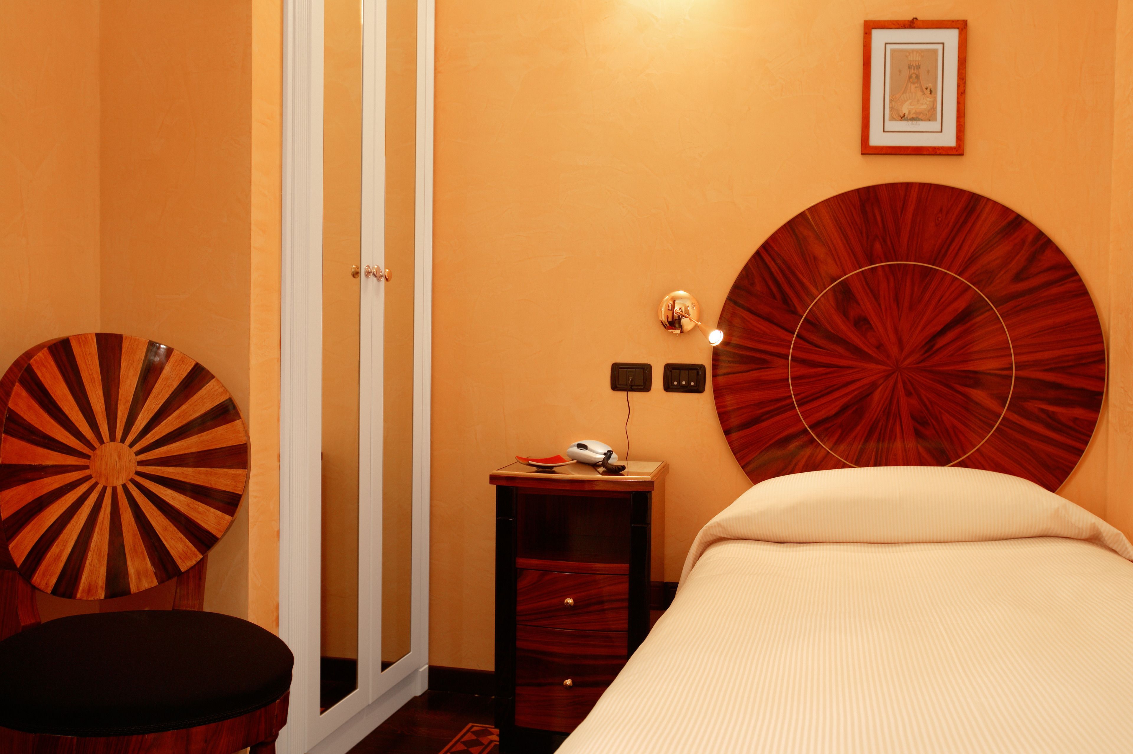 A hotel room with a bed, a desk with a computer, a chair, and a large circular artwork on the wall.