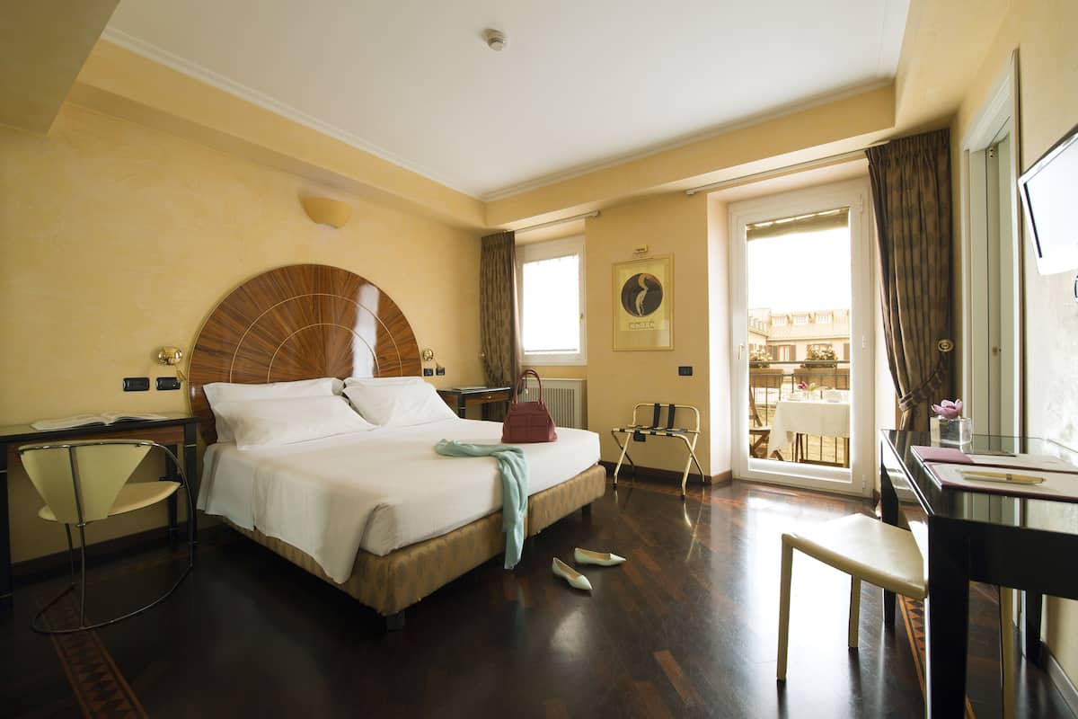 Habitación de hotel con cama, escritorio, silla y vistas al exterior.