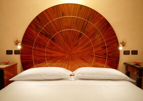 A bed with white linens, a large wooden headboard with a radial design, and two bedside tables with lamps.