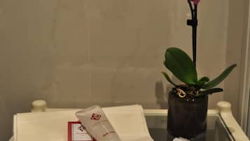 Un bagno con asciugamano, flacone di schiuma da bagno e orchidea in vaso.