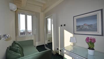 Hotellihuone, jossa on sänky, työpöytä, lamppu, ruukussa oleva kasvi ja seinällä oleva kehystetty kuva.