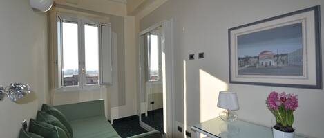 Una habitación de hotel con una cama, un escritorio, una lámpara, una planta en maceta y un cuadro en la pared.