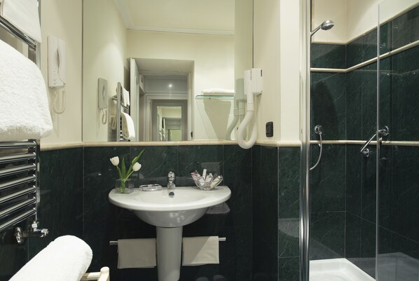 Un baño moderno con un lavabo blanco, cabina de ducha con mampara de vidrio y teléfono a la vista.