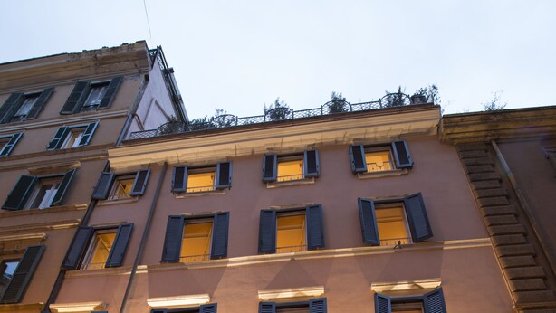 Una entrada de hotel con fachada de piedra, varias ventanas con contraventanas y un área de recepción bien iluminada.