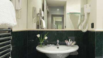 A bathroom with a white sink, a mirror, a telephone, and a glass vase with flowers.