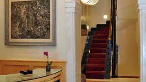 Una gran escalera con alfombra roja, una obra de arte enmarcada en la parte superior y un moderno mostrador de recepción con un jarrón de flores.
