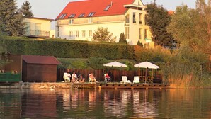 A lakeside property with a large house, outdoor seating by the water, and a dock. - Strandhotel Alte Donau (Vienna)