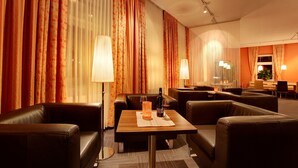 A hotel room with a seating area featuring a table with a bottle and glasses, surrounded by leather sofas. - Strandhotel Alte Donau (Vienna)