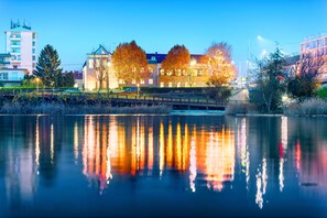 A calm lake reflecting buildings and trees, with a bridge in the foreground and a modern building with a flat roof in the background. - Strandhotel Alte Donau (Vienna)