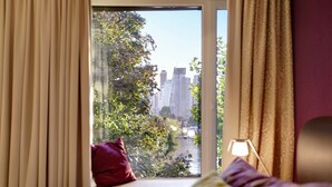A bedroom with a large window, a bed with pillows, and a bedside lamp. - Strandhotel Alte Donau (Vienna)