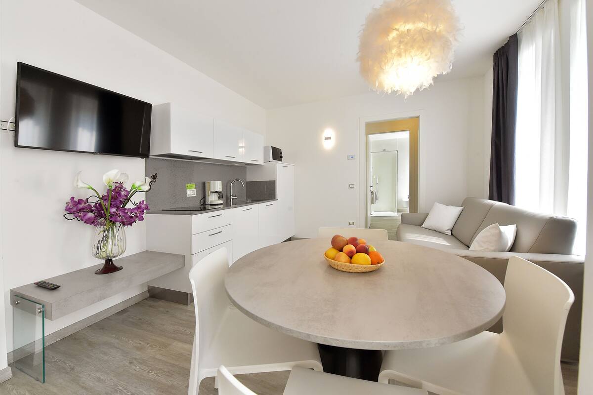 Eine moderne Küche mit Flachbildfernseher, einem Essbereich mit rundem Tisch und einer Couch.