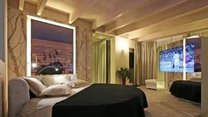 A modern hotel room with a large bed, a flat-screen TV, a large window with a sunset view, and a wooden ceiling.