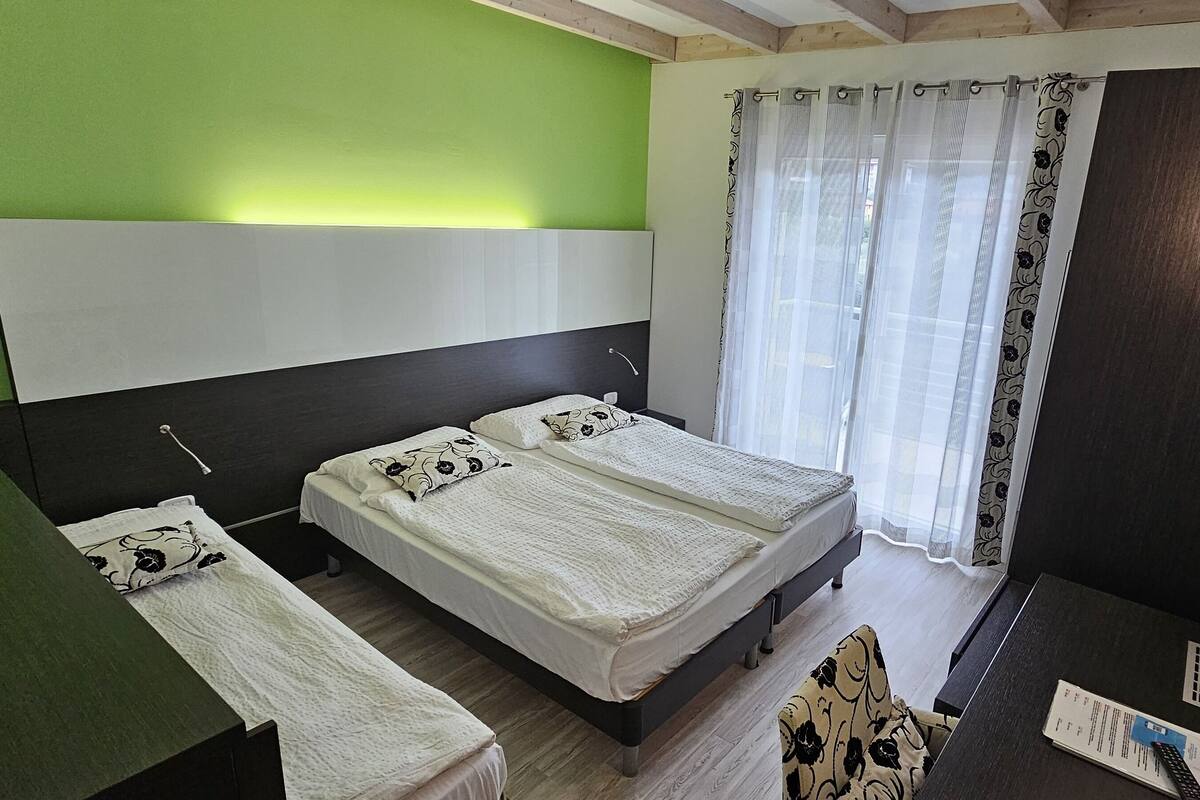 Ein Schlafzimmer mit zwei Betten, einem Schreibtisch, einem Stuhl, einem Fernseher und einem Fenster mit Vorhängen.