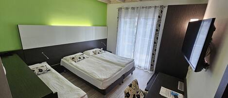 A bedroom with two beds, a desk, a chair, a TV, and a window with curtains.