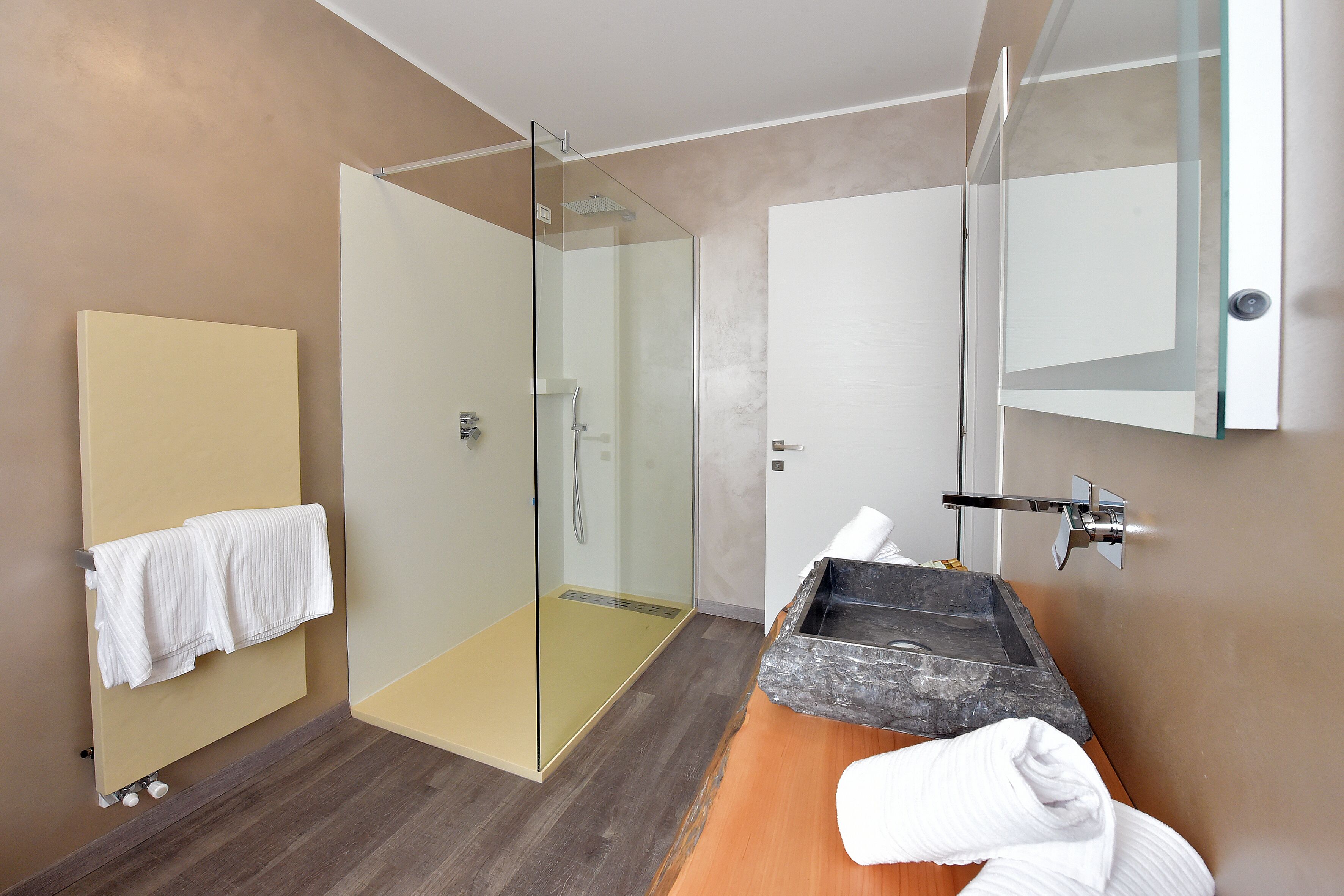 A modern bathroom with a glass shower enclosure, a wooden vanity with a stone sink, and a towel rack.