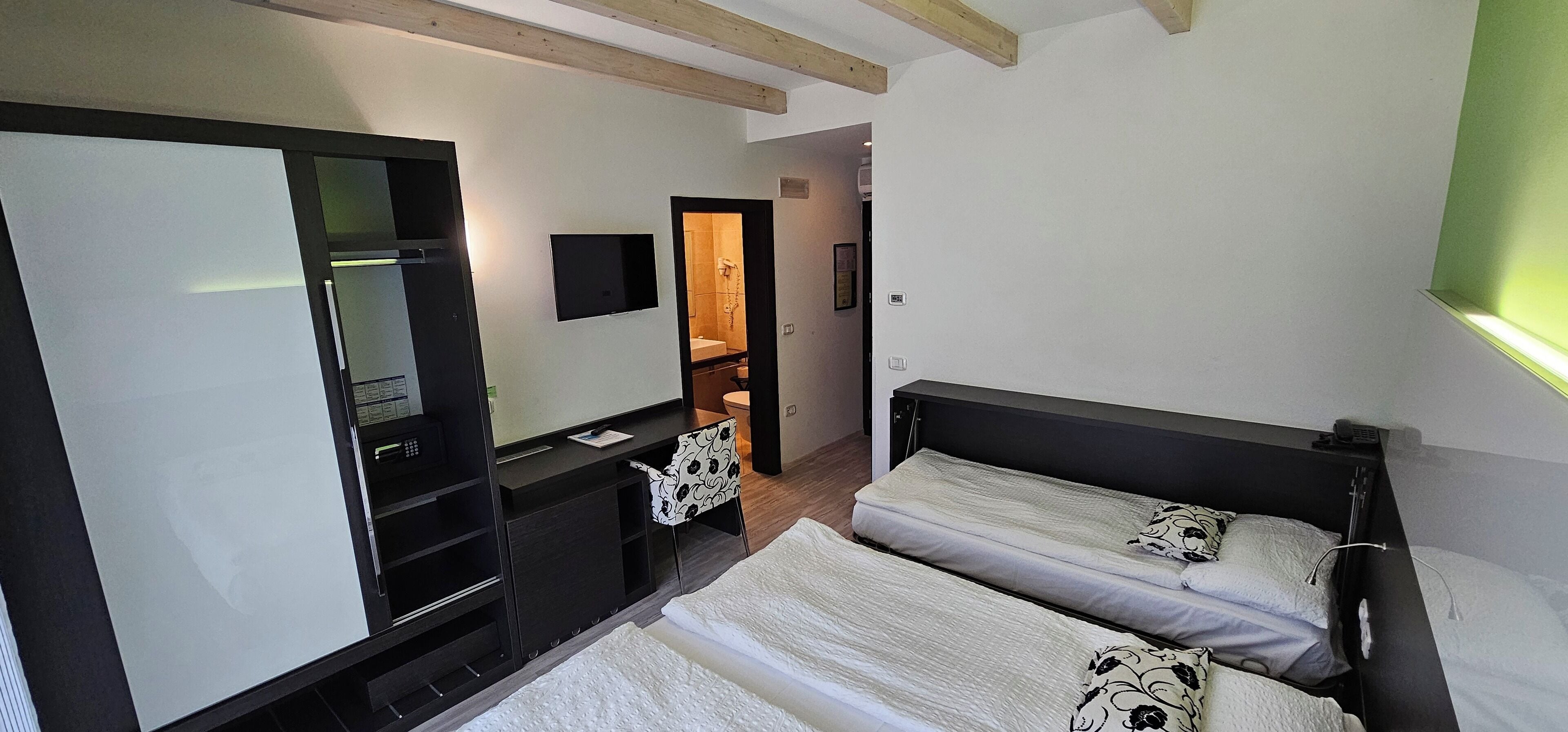 Une chambre d’hôtel de taille réduite, comprenant un lit, un bureau, une chaise, une télévision et une armoire.