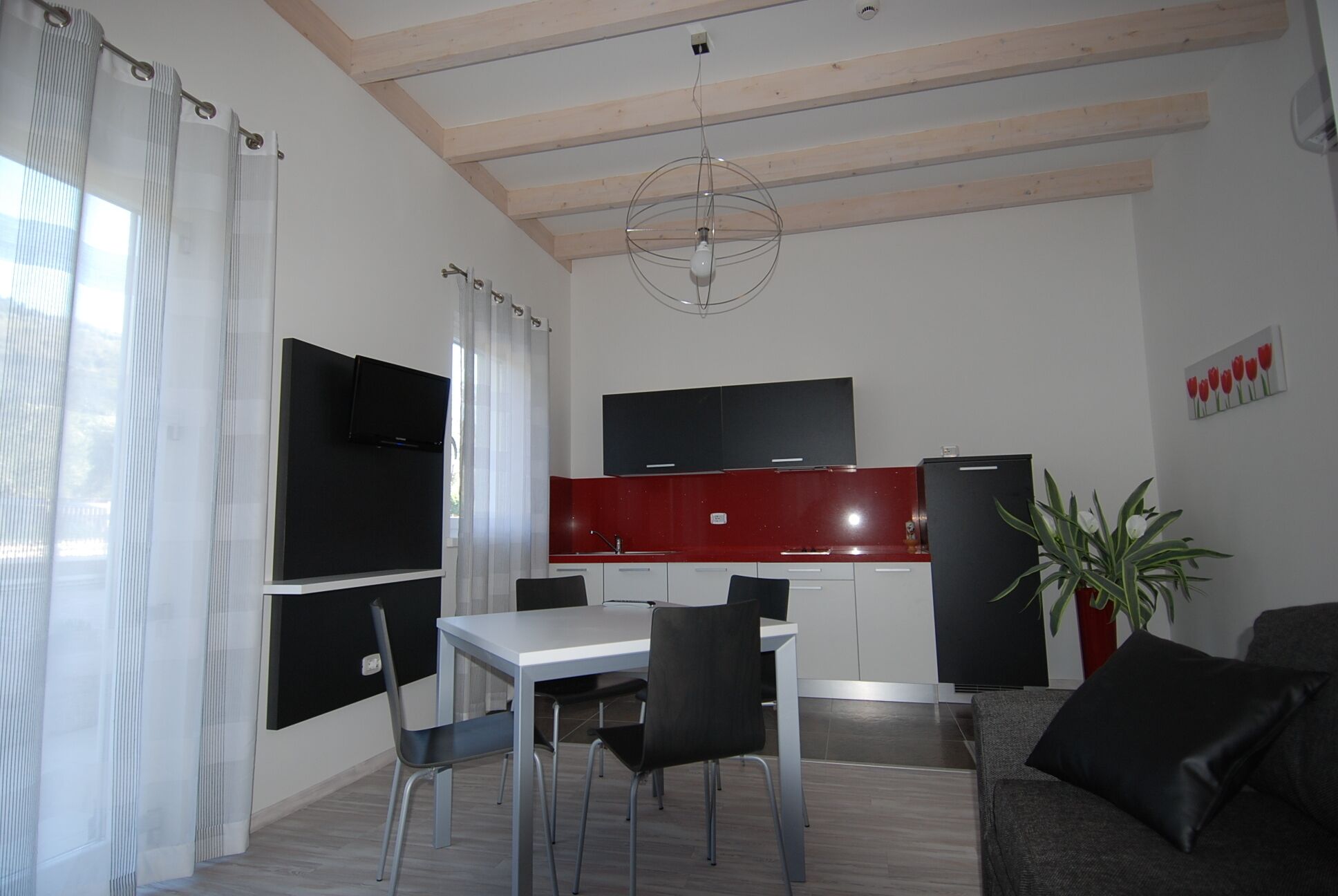A modern kitchen with a red countertop, a black refrigerator, and a dining area with a white table and black chairs.