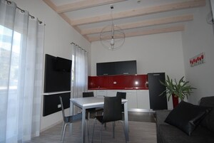 Una cocina moderna con encimera roja, refrigerador negro y comedor con mesa blanca y sillas negras.